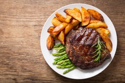 plate of grilled steak with rosemary, asparagus and potato on a wooden background, top view