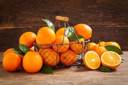 fresh orange fruits with leaves in a basket on a wooden background