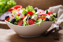 Bowl of fresh salad with vegetables, feta cheese and olives on a wooden table. Greek salad