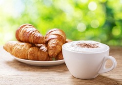 Cup of cappuccino coffee and croissants on wooden table