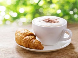 Cup of cappuccino coffee with croissant on wooden table