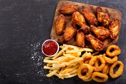 fast food products : onion rings, french fries and fried chicken on dark table, top view