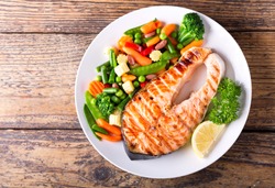 plate of grilled salmon steak with vegetables on wooden table, top view