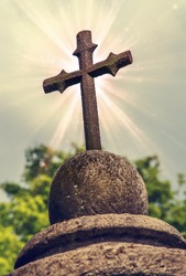 cast metal cross. element headstone carved from sand stone. old sculpture covered with moss. on sky background. soft selective  focus. vintage style. instagram toning effect
