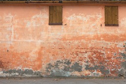 old wall with peeling paint, scratched stained plaster and closed windows - grunge background of urban decay

