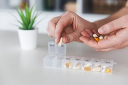 Female elderly hands sorting pills. Closeup of medical pill box with doses of tablets for daily take a medicine with white, yellow drugs and capsules. Young woman getting her daily vitamins at home. 