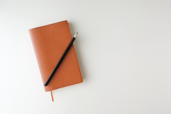 top view blank orange leather diary and pencil on white desk