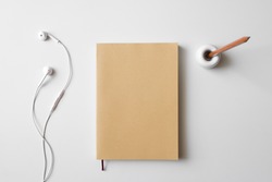 Top view blank book brown cover paper, earphone, and wood pencil in holder on white desk background