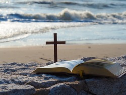 Open bible  and wood holy cross on stone with  blue sea as background. Love study bible.Bible is guide book of life. Christianity background concept.