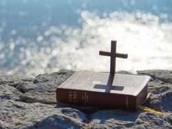 Holy Bible and wooden cross on stone with bokeh blue sea as background.Faith in God.Miracle from heaven.Believe in goddess.Love study bible.Bible is book of life.Christianity background concept.