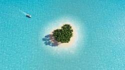 A heart-shaped paradise island in the middle of the ocean. Yacht approaching the island. Space for text