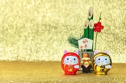 Japanese New Year's Greeting Card of a bamboo kadomatsu written congratulations, welcoming spring, a kagami mochi rice cake and two cat daruma figurines written good luck on a golden background.