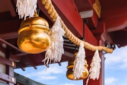 Shiny golden big suzu bells hung on a shimenawa rice or wheat straw rope adorned with suspended streamers known as shide and made with Japanese washi paper symbol of purity in a Shinto shrine.
