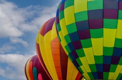 Isolated View of Three Colorful Abstract Patterned Hot Air Balloons against a backdrop of a Blue Sky with White Clouds