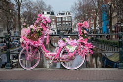 Old vintage woman bicycle decorated with pink flowers on small bridge in old part of Amsterdam