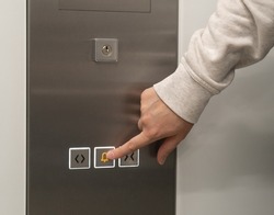 Lift emergency stop, alarm button button pressing. Elevator buttons pushing, forefinger pressing on down button, finger touching metal control panel on wall