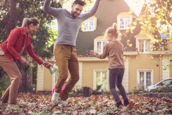 Happy family jumping at fall leaves at backyard. Have fun. 