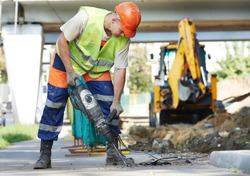 Builder worker with pneumatic hammer drill equipment breaking asphalt at road construction site