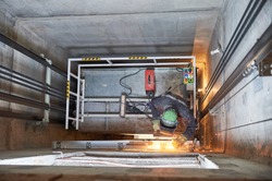 lift worker welding elevator fasteners in lift shaft