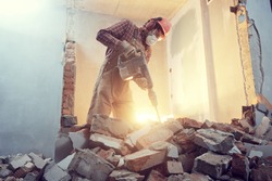 builder with hammer breaking wall indoors