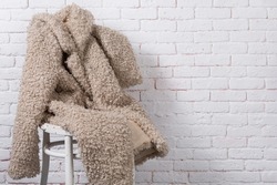 beige faux fur coat, as if sitting on a chair against a white brick wall, copy spase
