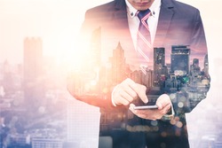 The double exposure image of the business man using a smartphone during sunrise overlay with cityscape image. The concept of modern life, business, city life and internet of things.