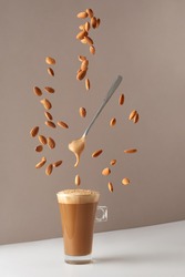 Glass cup with cappuccino and fragrant foam and a spoon and falling almonds. Cup with cappuccino, latte or coffee with milk. Creative design for cafes and restaurants with a cup of coffee. 