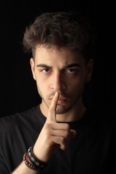 close-up portrait black background young male handsome model with hand shut up don't talk listen expression visual expression
