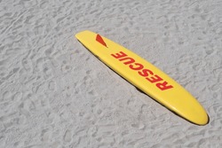 Yellow and red rescue surf board lying down on a beach in Galicia, Spain, ready for any emergency event at the sea