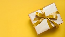 Gift box with golden satin ribbon and bow on yellow background.Holiday gift with Birthday or Christmas present, flat lay, top view, happy mother day copy space