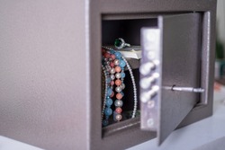 Money and jewelry in an open safe on the table. There is money and beads in the open safe.