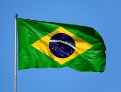 National flag of Brazil on a flagpole in front of blue sky