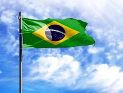 National flag of Brazil on a flagpole in front of blue sky.