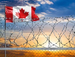 A fence with barbed wire against the background of a colorful sky and a flagpole with the flag of Canada protects the state's border from illegal migration.