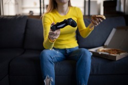 Close up cute girl plays the game on the console and eats pizza