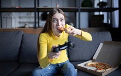 Cute girl plays the game on the console and eats pizza
