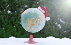 globe with christmas hat on snow. bokeh flare Santa Claus Hat on ball. International Christmas. universe travel concept