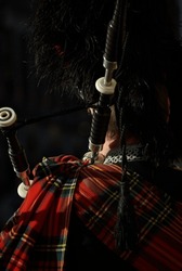 Scottish bagpiper in traditional red and black tartan dress, Edinburgh, scotland
