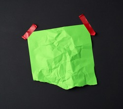 green crumpled sheet of paper glued with rubber red adhesive tape on a black background, copy space