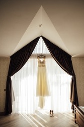 The bride's dress hangs on the window. A gentle bouquet of the bride and women's shoes stand on the windowsill