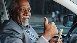 Elderly male sitting in car counting cash payment wages mature african american businessman calculates income successful business happy smiling man looking at camera shows thumbs up gesture approval