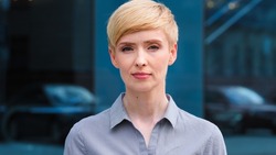 Close-up female serious face headshot portrait outdoors caucasian middle aged business woman boss blonde short haired lady wears formal shirt unhappy calm looking at camera standing posing on street