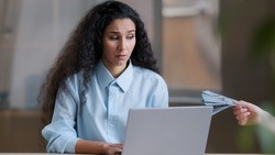 Upset arabian businesswoman worried executive worker hispanic girl freelancer work online on computer disappointed about financial problem unknown hand give payment dollars currency win monetary cash