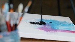 Close-up black dark paint splatters on canvas with pink and blue color picture female hand holding paint brush draws making texture creates masterpiece work of art painting preparing for exhibition