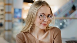 Close up emotional smiling flirting Caucasian 20s woman in eyeglasses lady girl blonde female in glasses indoors posing looking at camera businesswoman worker student model in shopping mall company
