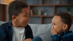 Two little boys friendly talking laughing at home. Ethnic African American multiracial multiethnic male kids schoolboys pupils sons indoors talk laugh together. Children brothers friends conversation
