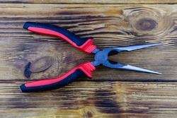 Needle nose pliers with red handles on wooden background. Top view