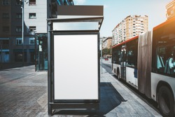 An empty poster mock-up on an outer side of the bus stop; advertising billboard placeholder template on the stop of public transport with a bus on the right; a mockup of a blank white outdoor banner