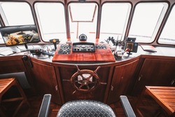 A cockpit area inside of a deckhouse of a retro safari or cruise yacht with a control panel on the wooden base and many navigation devices: compass, radio transceiver, radars, surveillance, dashboards