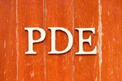 Alphabet letter in word PDE (abbreviation of permitted daily exposure, partial differential equation or personal development education) on old red color wood plate background